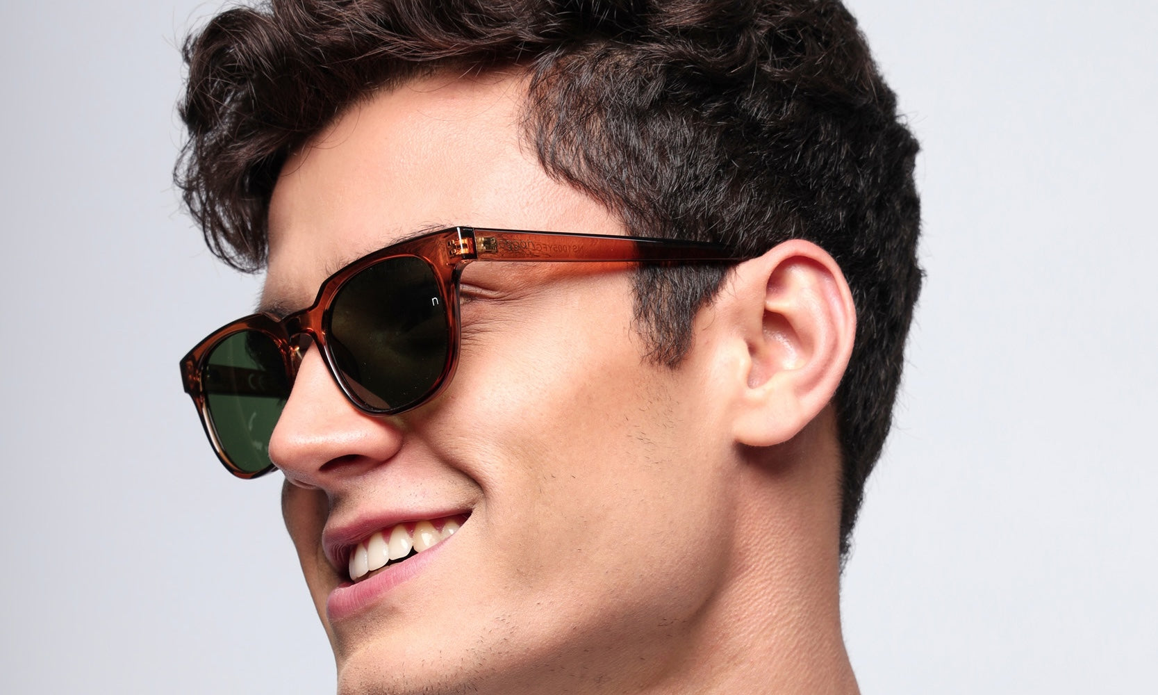 Model wearing Aura Desert Flame sunglasses (NS1005YFGL) with warm brown polycarbonate frame and scratch-resistant glass lenses under golden sunlight